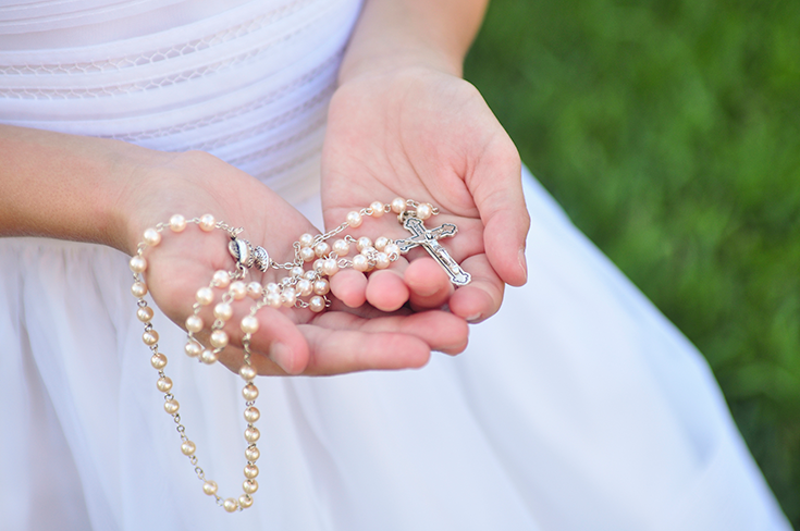 A close up a a girl in a white confirmation dress holding rosary beads.